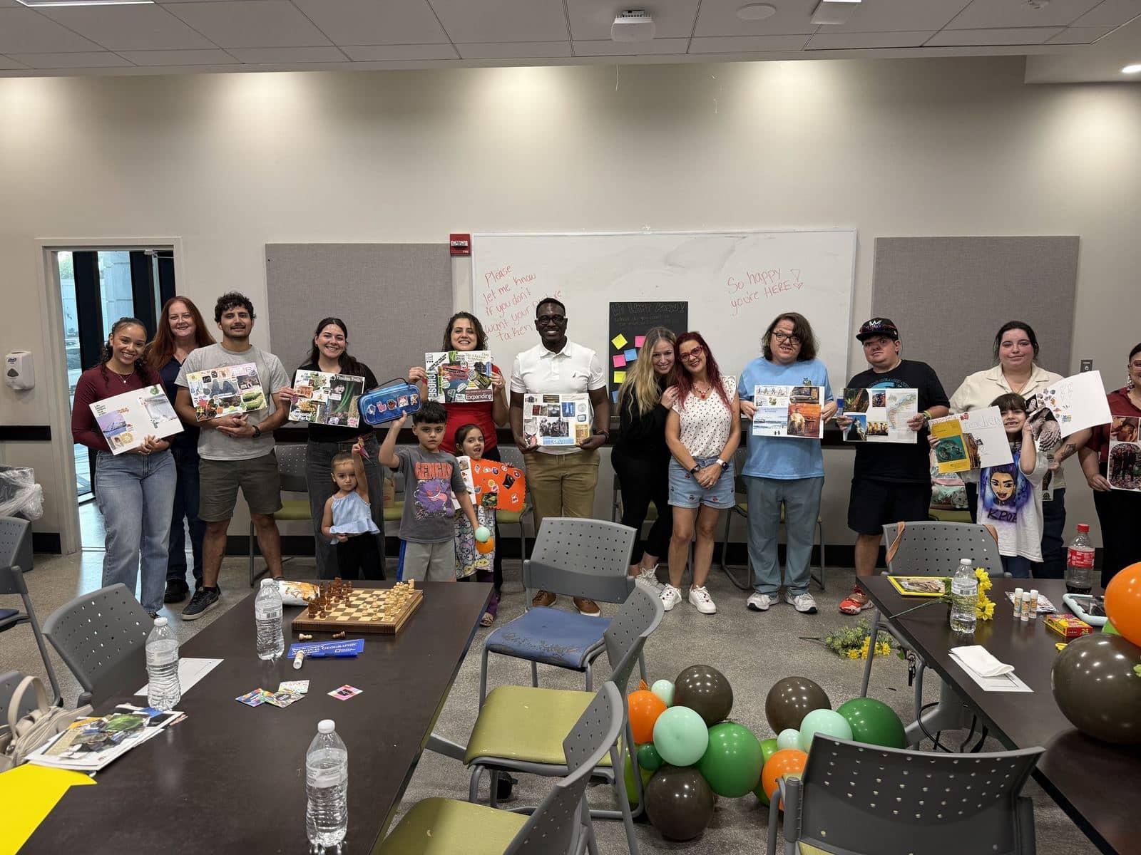 A large group of ACES participants, families, and staff standing together holding up the vision boards they created at a community workshop