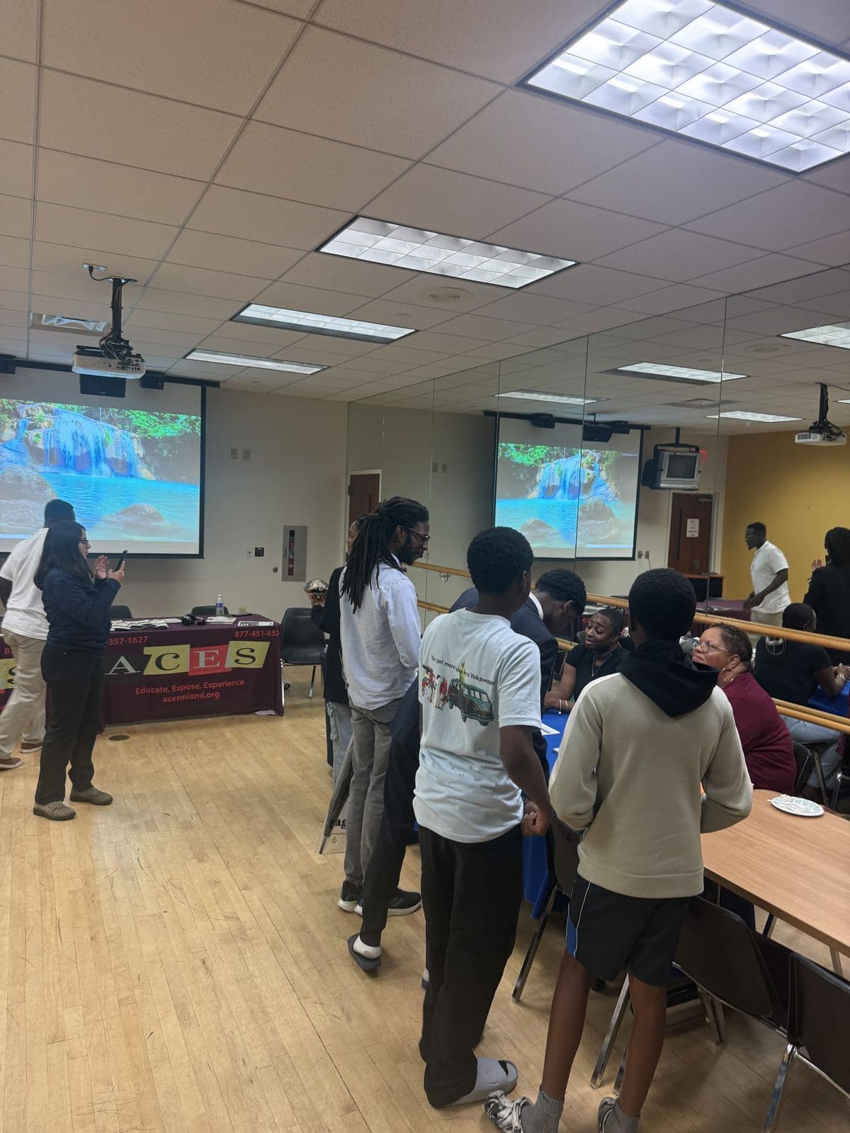 Participants gathered around the ACES information table during a presentation, with program slides on screen behind them