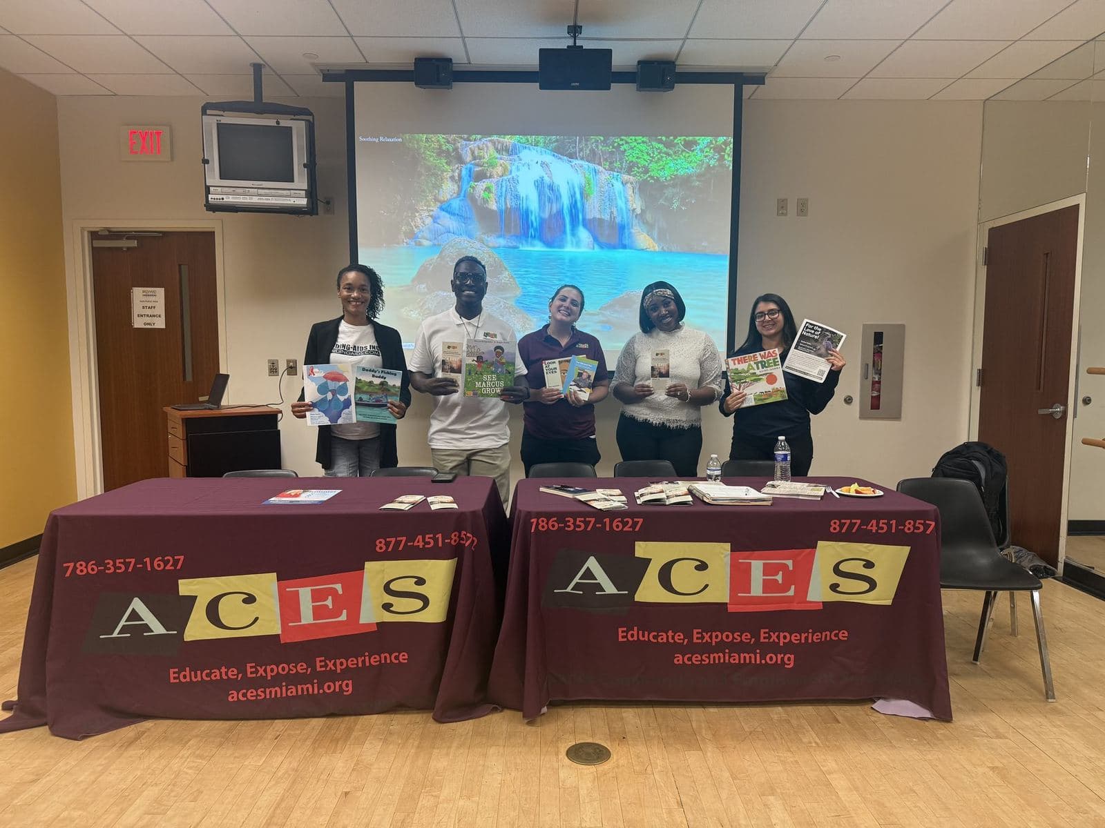 Five members of the ACES team standing behind two ACES-branded tables holding program brochures at a community resource event