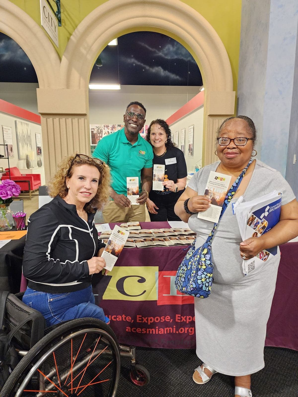Community members, including a woman using a wheelchair, gathered at the ACES resource table collecting information