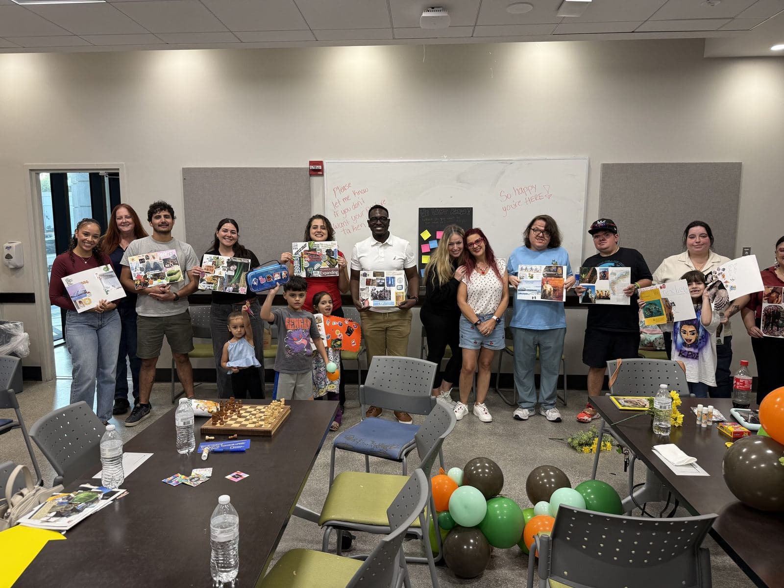 A large group of ACES participants, families, and staff standing together holding up the vision boards they created at a community workshop